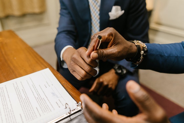 One person reaching across a desk to hand a pen t another person